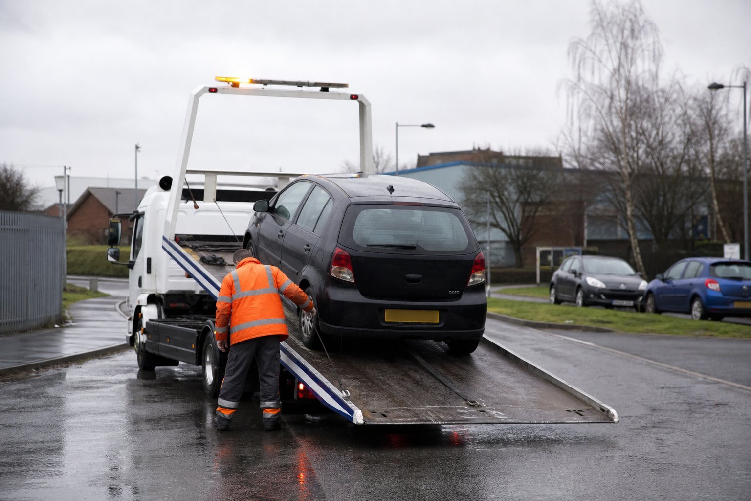 Recovery operator loading a car onto a flatbed truck in wet conditions